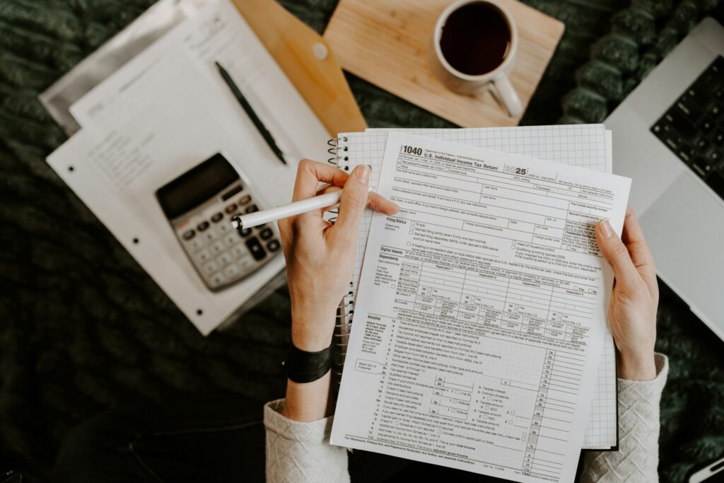 Person calculating figures on tax paperwork with a calculator, notebook, and coffee